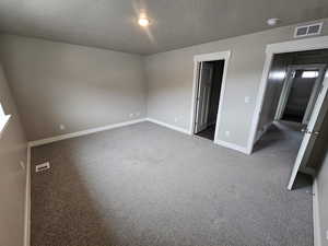 Unfurnished bedroom featuring baseboards, dark colored carpet, visible vents, and a textured ceiling