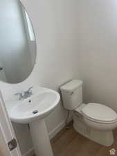 Half bathroom featuring wood finished floors, toilet, and baseboards