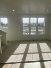 Carpeted empty room with visible vents, baseboards, stairway, and a healthy amount of sunlight