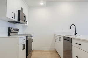 Kitchen featuring light stone counters, a sink, light wood-type flooring, stainless steel appliances, and white cabinetry