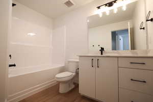 Bathroom with  shower combination, toilet, visible vents, wood finished floors, and vanity