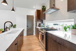 Kitchen featuring wall chimney exhaust hood, stainless steel gas range, light countertops, light wood-type flooring, and decorative light fixtures