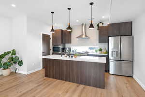 Kitchen with stainless steel appliances, light countertops, dark brown cabinetry, wall chimney range hood, and recessed lighting