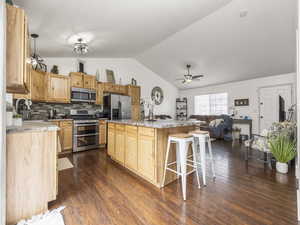 Kitchen featuring a ceiling fan, a sink, a breakfast bar area, lofted ceiling, and appliances with stainless steel finishes
