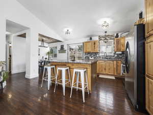 Kitchen featuring a sink, vaulted ceiling, freestanding refrigerator, a kitchen bar, and a kitchen island