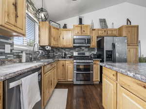 Kitchen featuring dark wood-style floors, stainless steel appliances, vaulted ceiling, a sink, and tasteful backsplash