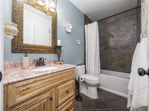 Full bath featuring shower / tub combo, vanity, stone finish floor, and toilet