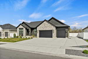 View of front of house featuring a front lawn, stone siding, concrete driveway, fence, and an attached garage