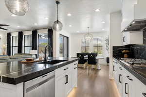 Kitchen with wall chimney exhaust hood, a sink, dark countertops, recessed lighting, and appliances with stainless steel finishes