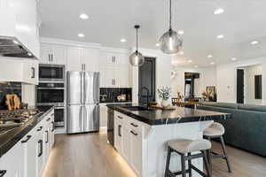 Kitchen featuring wall chimney range hood, a sink, stainless steel appliances, a kitchen bar, and recessed lighting