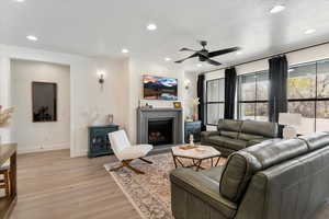 Living room featuring baseboards, recessed lighting, light wood-style floors, a ceiling fan, and a lit fireplace