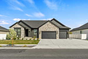 View of front facade featuring board and batten siding, an attached garage, fence, and stone siding