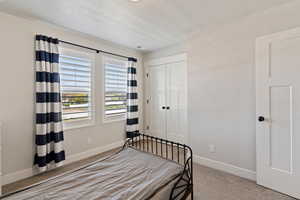 Bedroom featuring carpet, baseboards, a textured ceiling, and a closet