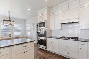 Kitchen featuring dark countertops, appliances with stainless steel finishes, backsplash, a notable chandelier, and dark wood-style floors