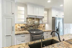 Kitchen with white cabinets, backsplash, a sink, glass insert cabinets, and appliances with stainless steel finishes