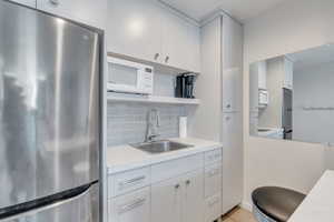 Kitchen featuring light countertops, a sink, white microwave, and freestanding refrigerator