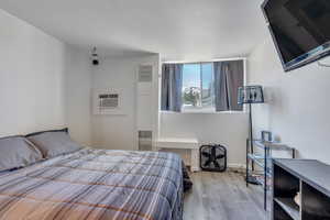 Bedroom with baseboards, wood finished floors, and a wall mounted AC