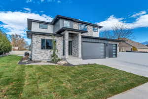 Contemporary house featuring concrete driveway, stone siding, and an attached garage