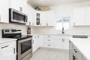 Kitchen featuring white cabinets, light countertops, a sink, glass insert cabinets, and appliances with stainless steel finishes