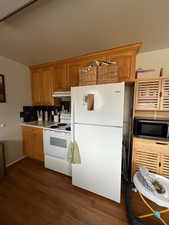 Kitchen featuring dark wood finished floors, backsplash, white appliances, brown cabinets, and under cabinet range hood