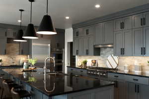 Kitchen featuring hanging light fixtures, decorative backsplash, gray cabinetry, dark stone countertops, and recessed lighting