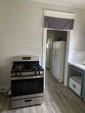 Kitchen featuring white fridge with ice dispenser, light wood-style floors, stainless steel range with gas stovetop, and light countertops