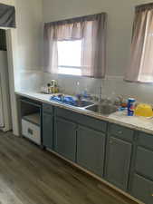 Kitchen with green cabinetry, dark wood-style floors, light countertops, a sink, and refrigerator