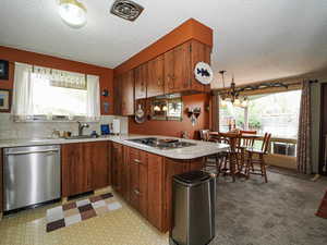 Kitchen with a textured ceiling, a sink, stainless steel appliances, light countertops, and a peninsula