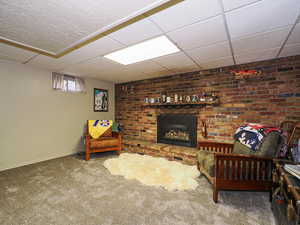 Living room with a paneled ceiling, a brick fireplace, carpet flooring, and baseboards