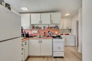 Kitchen with open shelves, a sink, light wood-style floors, white appliances, and white cabinets