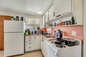 Kitchen featuring open shelves, a sink, white appliances, light countertops, and white cabinets