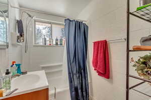 Full bathroom featuring concrete block wall, a healthy amount of sunlight, vanity, and shower / bath combo with shower curtain