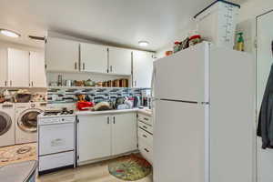 Kitchen featuring white cabinets, white appliances, washer and dryer, light wood finished floors, and backsplash