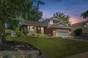 View of front of house with brick siding, a lawn, fence, and driveway