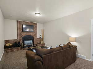 Living room with a textured ceiling, carpet, baseboards, a brick fireplace, and visible vents