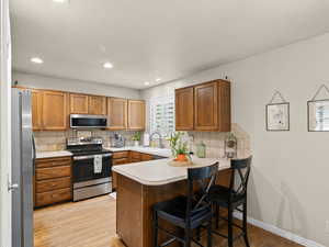Kitchen with stainless steel appliances, light countertops, light wood-style flooring, a peninsula, and tasteful backsplash