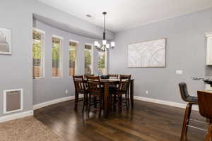 Dining room featuring dark wood-type flooring, visible vents, baseboards, and an inviting chandelier