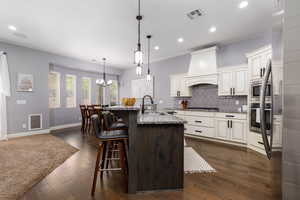 Kitchen with custom exhaust hood, a sink, stainless steel appliances, a kitchen bar, and visible vents