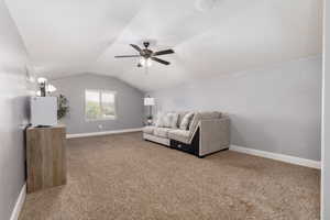 Carpeted living area featuring ceiling fan, lofted ceiling, and baseboards
