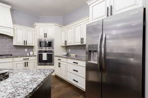 Kitchen featuring dark wood finished floors, tasteful backsplash, light stone countertops, and appliances with stainless steel finishes