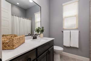 Full bath featuring tile patterned flooring, toilet, vanity, baseboards, and a shower with shower curtain