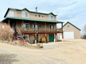View of front of home with a garage, driveway, an outbuilding, stone siding, and a deck