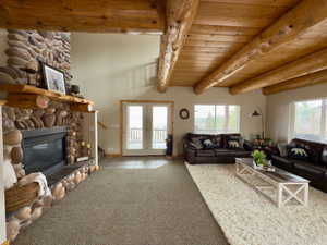 Carpeted living room featuring baseboards, beam ceiling, a stone fireplace, and a wealth of natural light
