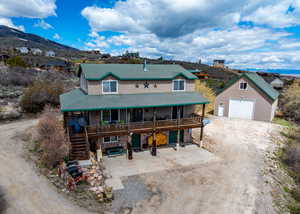 View of front of house featuring a garage, stone siding, roof with shingles, dirt driveway, and an outbuilding