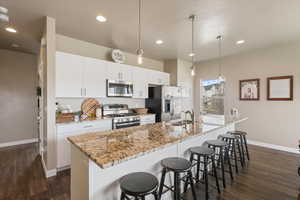 Kitchen featuring a kitchen island with sink, a sink, baseboards, dark wood-type flooring, and appliances with stainless steel finishes
