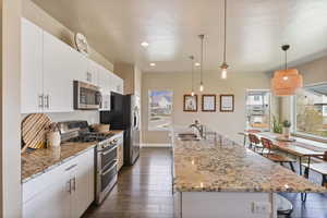 Kitchen featuring a sink, a breakfast bar, stainless steel appliances, a center island with sink, and dark wood finished floors