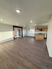 Unfurnished living room with baseboards, a textured ceiling, and dark wood-style floors