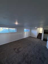 Carpeted empty room featuring stairs, a textured ceiling, and plenty of natural light