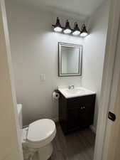 Half bathroom with baseboards, wood finished floors, toilet, and vanity