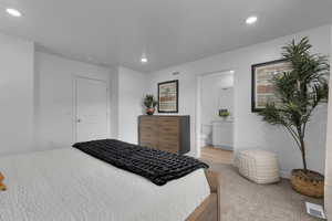 Bedroom with ensuite bathroom, visible vents, recessed lighting, and light colored carpet